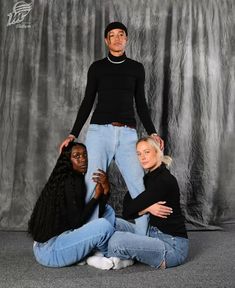 three people posing for a photo in front of a gray backdrop with the same person standing behind them