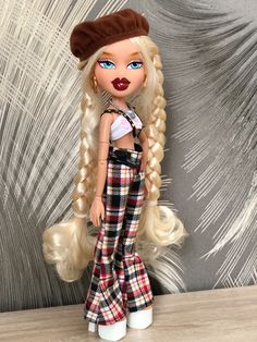 a doll with long blonde hair wearing plaid pants and a brown hat on top of a wooden table