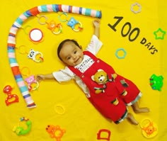 a baby laying on top of a yellow blanket with toys around it and the words 100 days written in large letters