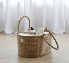 a wicker basket with two dolls in it on the floor next to a window