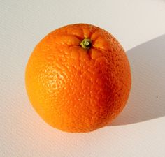 an orange sitting on top of a white table next to a shadow from the sun