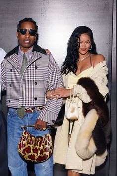 a man and woman standing next to each other in front of a wall holding purses