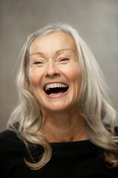 an older woman laughing and looking at the camera with her eyes closed, wearing a black shirt