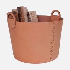 a brown leather bucket filled with logs and wood sticks on top of a white background