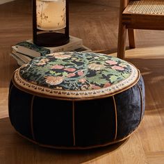 a round ottoman sitting on top of a hard wood floor next to a table with a lamp