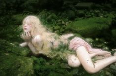 a woman laying on the ground covered in moss