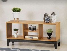 a wooden shelf with two plants and an alarm clock on top, in front of a white wall