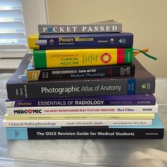 a stack of medical books sitting on top of a table next to a window with blinds