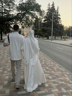 a man and woman dressed in white walking down the street with their backs to each other