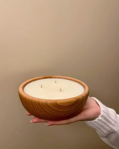 a person holding a wooden bowl with a candle in it and a wall behind them