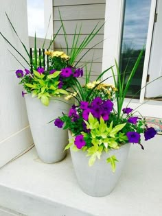 two white vases filled with purple and yellow flowers sitting on a front door step