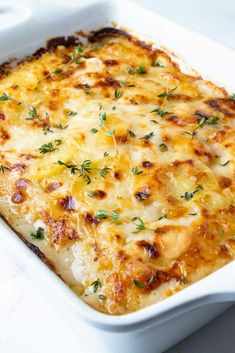 a casserole dish with cheese and herbs in it on a white countertop