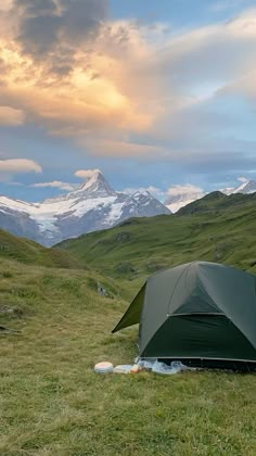 a tent pitched up in the grass with mountains in the background