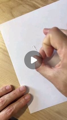 someone is cutting out a piece of paper on top of a wooden table with scissors