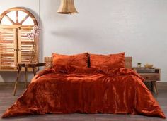 a bed with an orange comforter and pillows in front of a wooden table next to a window