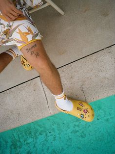 a person wearing yellow rubber shoes with tattoos on their legs and feet, while sitting in a chair