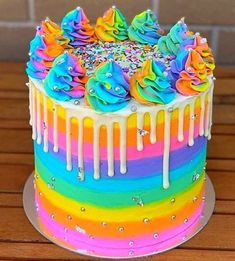 a multicolored cake with icing and sprinkles sitting on top of a wooden table