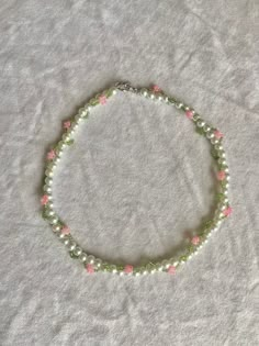 a green and pink beaded necklace on a white sheet with silver clasp closures