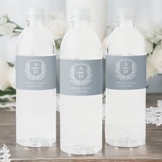 three water bottles with labels on them sitting on a table next to white flowers and lace