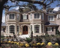 a large house with lots of windows and landscaping around the front door, along with yellow flowers