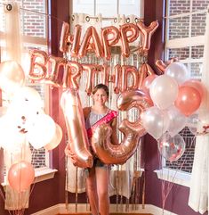 a woman holding balloons in front of a happy birthday sign