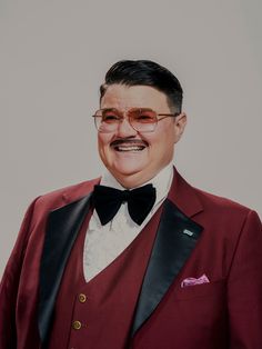 a man in a tuxedo and bow tie is smiling at the camera while wearing glasses