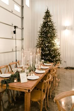 a dining table set for christmas dinner with candles on it and a tree in the background