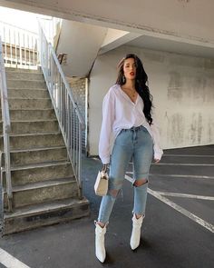 a woman standing in an empty parking lot wearing ripped jeans and white high top sneakers