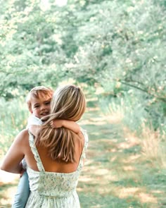 a woman holding a child in her arms while walking down a path through the woods