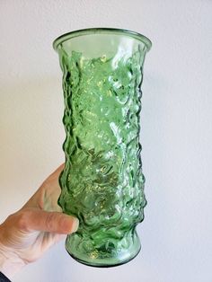 a hand holding a green glass vase in front of a white wall