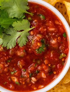 a bowl of salsa with tortilla chips and cilantro on the side