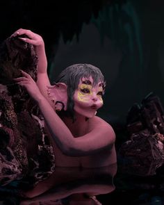 a woman with painted face and body poses in front of some rocks, while holding onto a rock