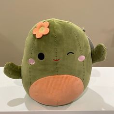 a green stuffed animal with a flower on it's head sitting on a table