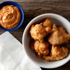 a bowl filled with tater tots next to a cup of dip