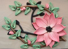 a pink flower with green leaves is on the wall next to a black metal hook