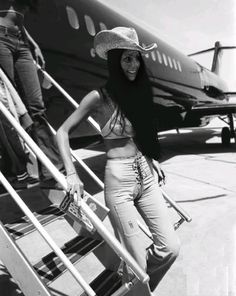 a woman standing in front of an airplane on the tarmac with her hat over her head