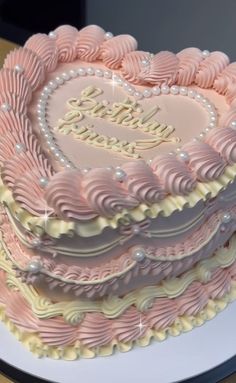 a heart shaped birthday cake with pink frosting and white icing, on a plate