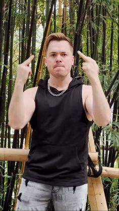 a man standing in front of bamboo trees making the middle finger sign with his fingers