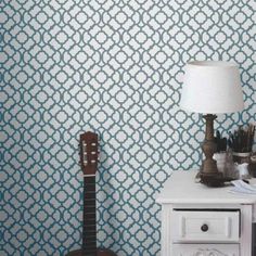 a guitar sitting on top of a white table next to a lamp and wall paper