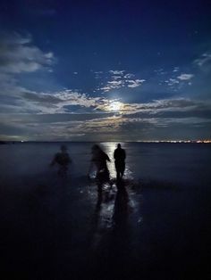 two people standing on the beach at night with the moon in the sky above them