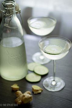 two glasses filled with liquid and sliced cucumbers next to a bottle on a table