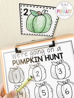 a hand holding a marker next to a pumpkin hunt sign with numbers and pictures on it