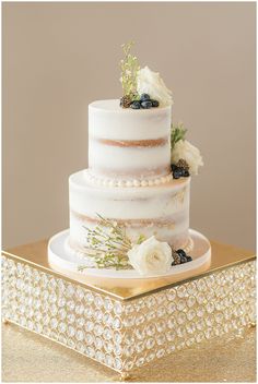 a three tiered cake with flowers and berries on top sits on a gold tray