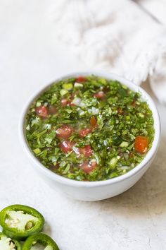 a white bowl filled with green vegetable soup next to some sliced jalapenos