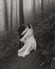 a bride and groom walking through the woods in black and white photo by wedding photographer