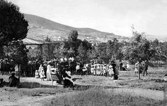 an old black and white photo of people standing in the grass with mountains in the background