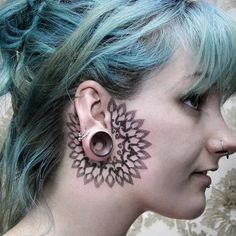 a woman with blue hair has tattoos on her face and behind her ear is a flower