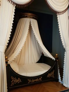 a canopy bed with white drapes on it's sides and gold trimmings