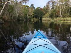 a blue kayak in the middle of a river surrounded by trees and water with no one on it