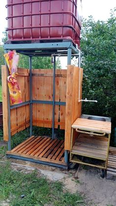 an outdoor shower made out of wooden pallets and metal frame with a red bucket on top